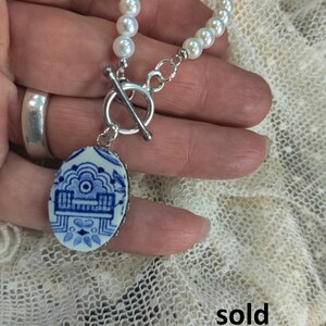 May include: A white pearl necklace with a silver toggle clasp and a blue and white porcelain pendant. The pendant features a traditional Chinese design. The necklace is sold.