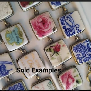 May include: A close-up of a bracelet made with vintage china tiles. The tiles feature floral patterns, blue and white designs, and text that reads "Teito China Made in Japan". The bracelet is made with brass hardware and has a clasp.