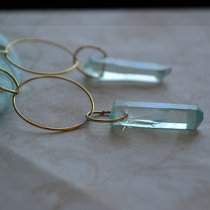 May include: A pair of gold hoop earrings with a light blue crystal pendant on each hoop.