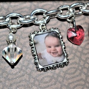 May include: A silver charm bracelet with various charms, including a heart charm with the word "love" on it, a clear crystal charm, a photo charm with a baby's picture, a red heart charm, and a silver charm with the name "Emily" on it.