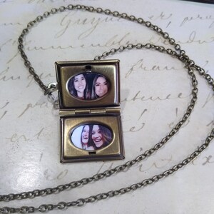 May include: A gold locket necklace with a chain. The locket is open and has two oval-shaped photos inside. The photos show two women smiling.