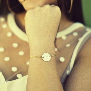 May include: A gold chain bracelet with a round pendant featuring the letter "A" on a white background.