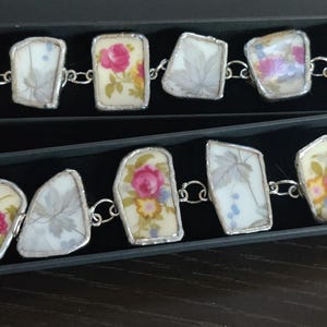 May include: Two bracelets made with vintage china, each with a silver chain and seven different pieces of china. The china pieces are various shapes and sizes and feature floral patterns.