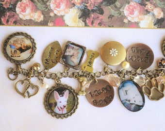 May include: A charm bracelet with various charms, including dog paw prints, a heart, a bone, and several round charms with photos of dogs and dates. The charms are attached to a silver chain.