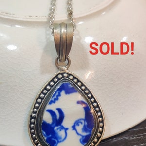 May include: A silver teardrop-shaped pendant necklace with a blue and white porcelain cameo featuring two birds. The cameo is surrounded by a silver beaded border. The word "SOLD!" is written in red letters on a white background.