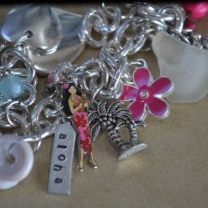 May include: A silver charm bracelet with various charms, including a palm tree, a flower, a seashell, and a tag that says "Aloha".