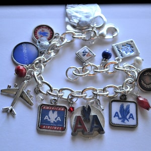 Puede incluir: Un brazalete de plata con varios abalorios, incluyendo un peque&ntilde;o avi&oacute;n, cuentas rojas y azules, y abalorios con el logotipo de American Airlines. El brazalete tambi&eacute;n tiene un abalorio con las palabras "oneworld" y un abalorio con una corona.
