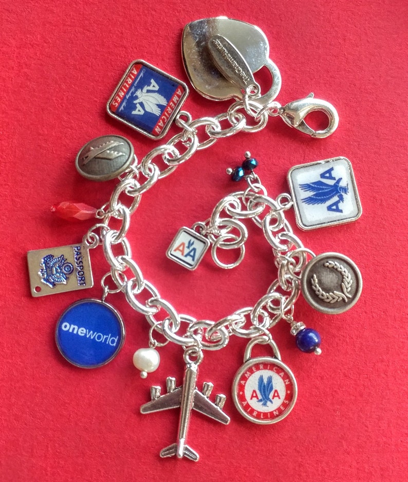 Puede incluir: Un brazalete de plata con varios dijes, incluyendo un coraz&oacute;n, un avi&oacute;n y varios dijes con el logotipo de American Airlines. Los dijes est&aacute;n en una cadena de plata con un cierre de langosta.