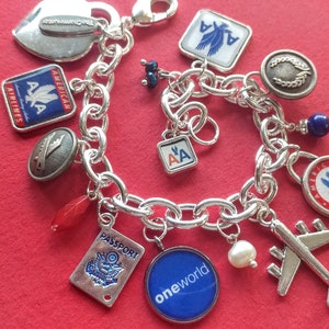 Puede incluir: Un brazalete de plata con varios dijes, incluyendo un coraz&oacute;n, un pasaporte, un avi&oacute;n y varios dijes con el logotipo de American Airlines. Los dijes est&aacute;n unidos a una cadena de plata.