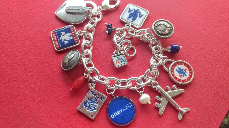 Puede incluir: Un brazalete de plata con varios dijes, incluyendo un coraz&oacute;n, un pasaporte, un avi&oacute;n y varios dijes con el logotipo de American Airlines. Los dijes est&aacute;n unidos a una cadena de plata.