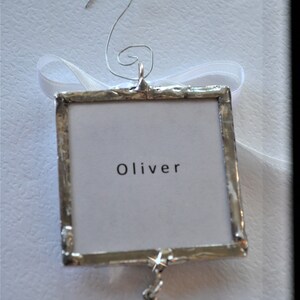May include: Silver-toned ornament with a white card that says "Oliver" and a silver bone charm.