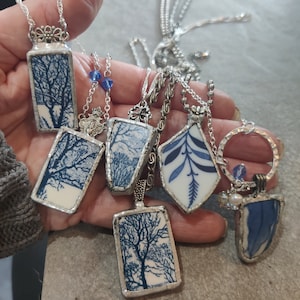May include: A collection of seven necklaces with blue and white porcelain pendants featuring tree and floral designs. The pendants are framed in silver and hang from silver chains.