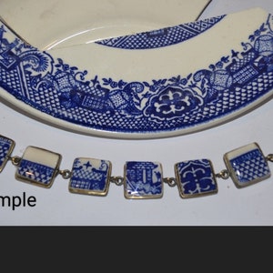 May include: A blue and white porcelain bracelet with a silver clasp. The bracelet is made from pieces of a broken plate with a blue and white floral pattern. The word "Example" is written below the bracelet.