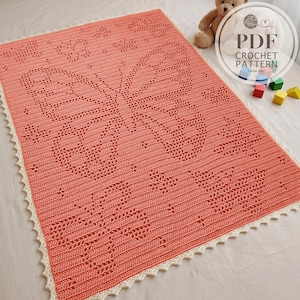 Puede incluir: Una manta rectangular de ganchillo color coral con un intrincado patrón de mariposa creado con puntos calados. La manta está terminada con un delicado borde festoneado de color crema a lo largo de los cuatro lados, creando un contraste texturizado.