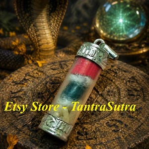 May include: A cylindrical glass pendant with silver-toned metal caps at both ends. Inside the clear glass tube are stacked layers of red, dark green, and light-coloured materials wrapped in white fibres. The text Etsy Store - TantraSutra is visible.