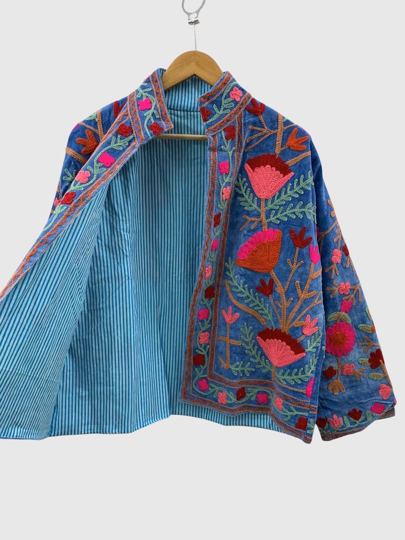May include: A blue jacket featuring vibrant floral embroidery in shades of pink, red, and orange. The garment has a stand-up collar and long sleeves, with an interior lining that displays a light blue and white vertical pinstripe pattern.