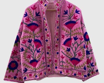 May include: A bright pink jacket featuring a high collar and long sleeves, adorned with intricate floral embroidery in shades of dark blue, magenta, and green. The garment is open at the front, revealing a light pink and white striped interior lining.