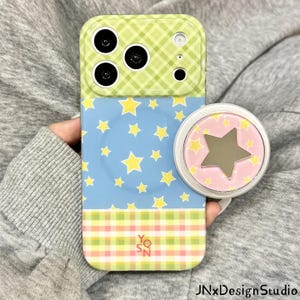 May include: A smartphone case featuring a green and white gingham top section, a blue middle section with yellow stars, and a pink and green gingham bottom section with the text YQSN. A circular phone grip with a pink background and a star mirror.