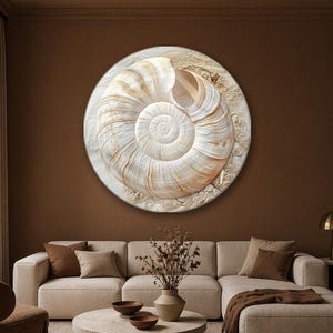 May include: A circular wall art piece featuring a large, detailed nautilus shell in shades of cream, beige, and soft brown. The shell is set against a textured, sandy-colored background that mimics the appearance of a beach or desert terrain.