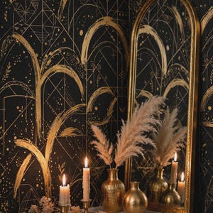 May include: A tall arched mirror with a gold frame stands against black wallpaper featuring gold geometric and brushstroke patterns. Two gold vases hold pampas grass, while two lit candles in gold holders sit nearby on a white marble surface.