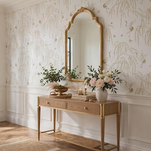 May include: A rectangular wooden console table with two drawers, gold-toned metal accents, and a lower cane shelf. Above the table hangs an arched mirror with a gold frame, set against white wallpaper featuring a gold crane and willow pattern.