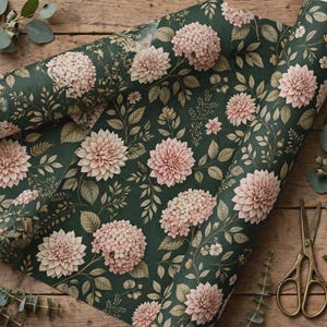 May include: A roll of wrapping paper featuring a dark green background with a repeating pattern of light pink dahlia flowers, hydrangea clusters, and green leaves. The paper is displayed alongside a pair of gold-toned metal scissors.