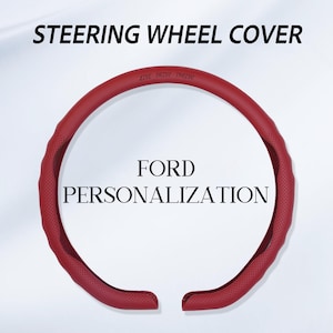 May include: A red steering wheel cover with a textured, perforated surface. The top section features the embossed text "LIVE DRIVE THRIVE". The text "STEERING WHEEL COVER" and "FORD PERSONALIZATION" appear in black lettering above and inside the ring.