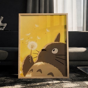 May include: A framed vertical art print featuring a brown, furry, large-eared creature holding a white dandelion. The background is a solid, warm yellow colour with several white dandelion seeds floating in the air around the creature.