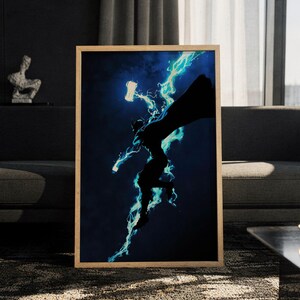 Könnte beinhalten: Ein gerahmter vertikaler Wandkunstdruck mit der dunklen Silhouette einer Figur mit Umhang, die durch die Luft springt. Die Figur ist von hellen, leuchtenden cyanfarbenen Blitzen umgeben und hält eine leuchtende hammerartige Waffe in der Hand.