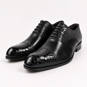 Può includere: Un paio di scarpe oxford nere che combinano pelle liscia e pannelli in pelle testurizzata con stampa coccodrillo sulla punta e sulla sezione dell'allacciatura. Le scarpe presentano sottili lacci neri e un tacco basso con finitura lucida.