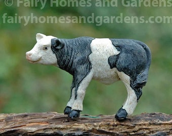 May include: Black and white miniature cow figurine. The cow is standing on a piece of wood.