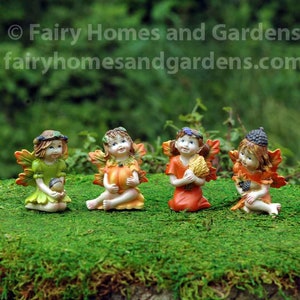 May include: Four miniature fairies with wings, dressed in autumn colors, holding fall harvest items. The fairies are sitting on a bed of green moss.