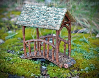 May include: A miniature wooden bridge with a green shingled roof. The bridge is made of brown wood and has a curved design. The bridge is sitting on a bed of green moss.
