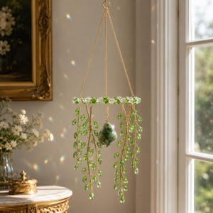 May include: A hanging mobile featuring a circular frame adorned with clear and green crystal beads. Suspended from the frame are multiple gold-toned wire strands decorated with green crystal leaves and a central teardrop-shaped green stone.