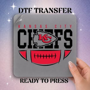 May include: A square DTF transfer sheet featuring the text DTF TRANSFER at the top and READY TO PRESS at the bottom. The center displays the Kansas City Chiefs logo in black and red, with a stylized red football graphic underneath on a gray background.