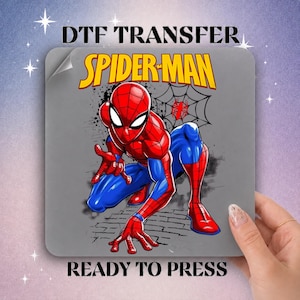 May include: A square DTF transfer sheet featuring a graphic of Spider-Man in a crouching pose. The character wears a red and blue suit with black webbing details. Above the character, the text reads SPIDER-MAN in yellow with black outlines.