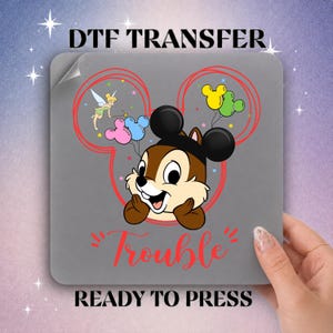May include: A DTF transfer sheet featuring a cartoon chipmunk wearing black mouse ears, surrounded by a red outline of a mouse head. It includes a small fairy, colorful balloons, and the red text "Trouble" with "DTF TRANSFER READY TO PRESS".