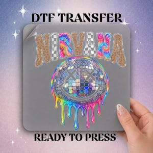 May include: A DTF transfer sheet featuring the text NIRVANA in a mix of leopard print, checkerboard, and tie-dye patterns. Below the text is a disco ball smiley face with X-shaped eyes and rainbow-colored paint dripping down.