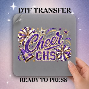 May include: A DTF transfer sheet featuring a graphic design with the text Cheer CHS in purple and gold glitter. The design includes two pom-poms, a megaphone with a star, and several small stars on a gray background with the text DTF TRANSFER READY TO PRESS.