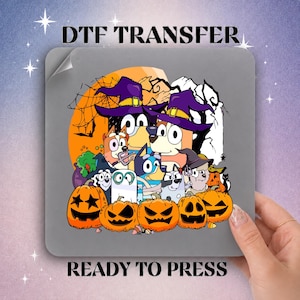 May include: A square DTF transfer sheet featuring a Halloween-themed graphic with cartoon dogs wearing purple witch hats. The design includes orange jack-o'-lanterns, a spider web, and a full moon background. The text DTF TRANSFER READY TO PRESS is visible.
