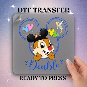 May include: A square DTF transfer sheet featuring a cartoon chipmunk wearing black mouse ears, holding blue, pink, yellow, and green balloons. Tinker Bell is flying above with a wand. The text reads DTF TRANSFER, Double, and READY TO PRESS.