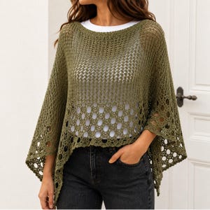 Op de afbeelding: Een olijfgroene gehaakte poncho met een opengewerkt breipatroon aan de bovenzijde en een groter cirkelvormig motief langs de onderzoom. Het kledingstuk heeft een brede boothals en een losvallend, gedrapeerd silhouet met puntige zijkanten.