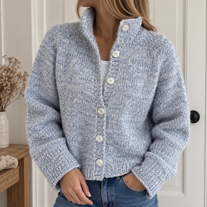 Peut inclure: Un cardigan en tricot épais dans un fil chiné bleu clair et blanc. Le cardigan présente un col montant, des manches longues avec des poignets côtelés et une fermeture boutonnée à l'avant avec six boutons blancs ronds sur un haut blanc.