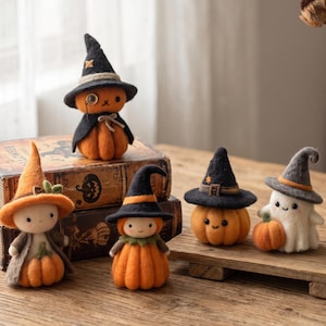 Op de afbeelding: Een verzameling van vijf naaldgevilte figuren, waaronder pompoenen, een spookje en personages met heksenhoeden. De figuren hebben texturen van oranje, zwarte en grijze wol met kleine geborduurde gezichtsdetails en decoratieve accenten.