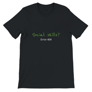 Peut inclure: Un t-shirt noir à manches courtes avec le texte Social skills? écrit dans une police verte manuscrite, suivi du texte Error 404 dans une police blanche sans empattement, centré sur la poitrine du vêtement.