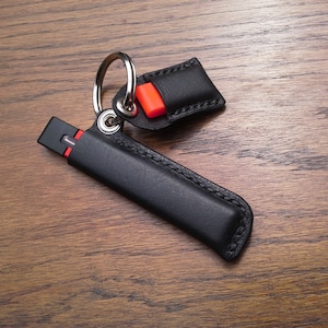 May include: A black leather keychain with a silver key ring and a red accent. The keychain has a small black leather pouch attached to it.