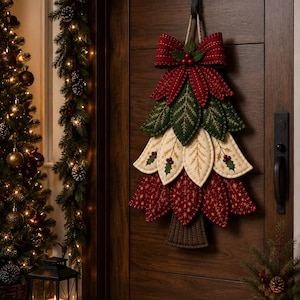 May include: A fabric wall hanging shaped like a Christmas tree, featuring layered leaves in red, cream, and dark green with stitched details. The tree is topped with a large red bow and small red berries, suspended by a twine loop from a black hook.