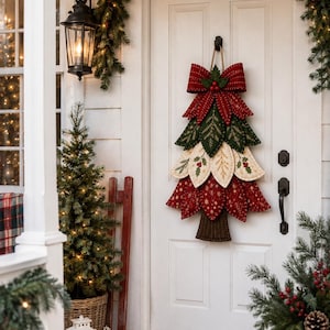 May include: A fabric Christmas tree door hanging decoration featuring layered, quilted leaves in red, green, and cream colors. The tree is topped with a large red bow and accented with holly berry motifs, hanging from a jute rope on a white door.