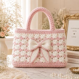 May include: A handmade crochet handbag featuring a shell stitch pattern in alternating rows of soft pink and white yarn. The bag has two sturdy top handles and a prominent, centered white crochet bow attached to the front exterior panel.