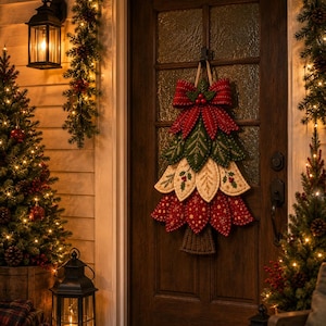 May include: A fabric Christmas tree wall hanging featuring layered, quilted leaves in red, green, and cream with embroidered details. The tree is topped with a large red bow and holly berries, suspended by a rope on a dark wooden door with glass panels.